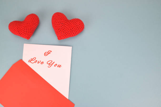 istock Red gift envelope with a declaration of love and two knitted hearts on a light blue background 1321428448