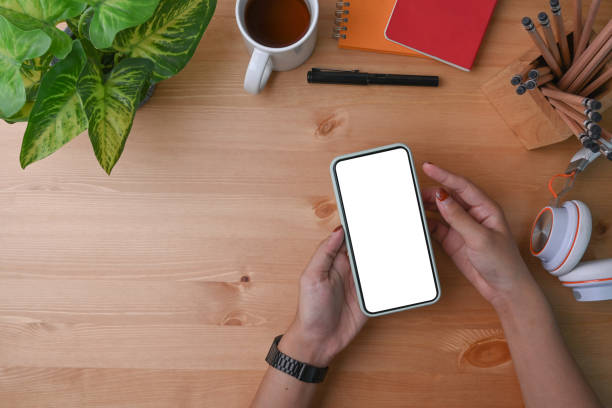 istock Above view woman holding mock up mobile phone on her workspace. 1321428540