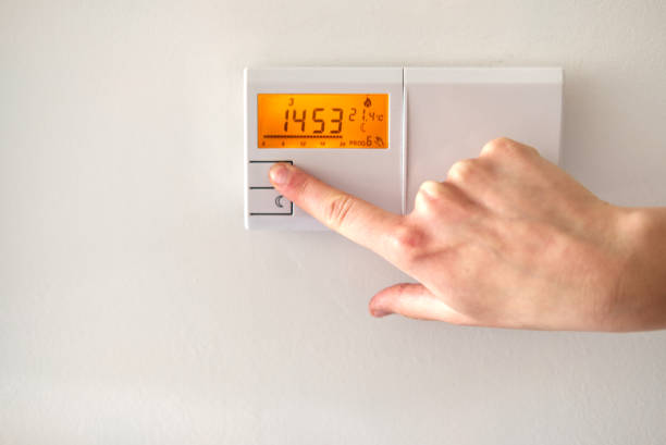 istock woman's hand operating electronic thermostat to adjust temperature at home 1321430768