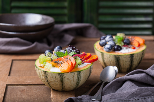 Healthy clean eating, dieting and nutrition, seasonal, summer breakfast concept. Fruit salad with yogurt in carved melon cantaloupe bowl on a kitchen table