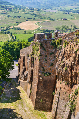 A suggestive view of the rock and tuff cliff of the ancient medieval town of Orvieto in the Umbria region, in central Italy, with a portion of the her valley. With a population of just 20,000 people, Orvieto is considered one of the most beautiful cities of art in Italy, founded since the Etruscan and Roman times on the flat top of a large butte of volcanic tuff. This same material was used for the construction of almost all the medieval houses and churches of Orvieto, as well as its famous Gothic-style Cathedral. Image in high definition format.