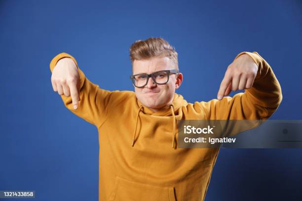 Young Handsome Man Dressed In Casual Yellow Sweater And Glasses On A Blue Background Surprised Pointing Down With His Finger With An Open Mouth And An Amazed Expression On His Face Stock Photo - Download Image Now