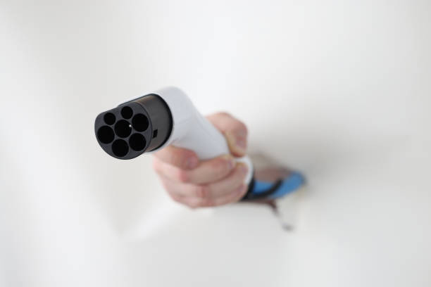 Hand through hole in white paper holds plug of electro car charging. Search for filling stations for electric vehicles concept
