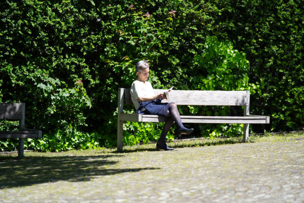 Elderly woman on park bench in front of St. Peter church reading a book. Photo taken June 1st, 2021, Zurich, Switzerland.