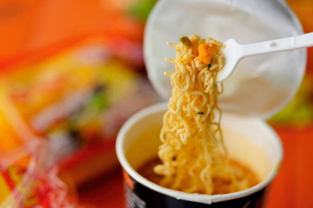 Asian fast food, available internationally, here a mouthful of freshly prepared, with boiling water, instant cup noodles on the provided foldable plastic fork, ready to be eaten. Shallow depth of field with the focus being on the noodles on the fork. Good copy space to the left of the image.