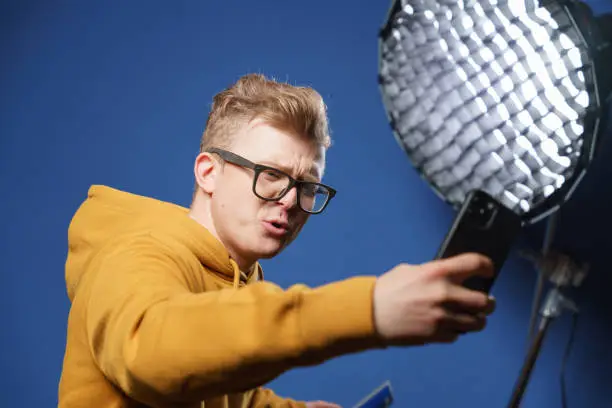 Photo of A blogger takes a selfie on the front camera of his phone in a professional studio.