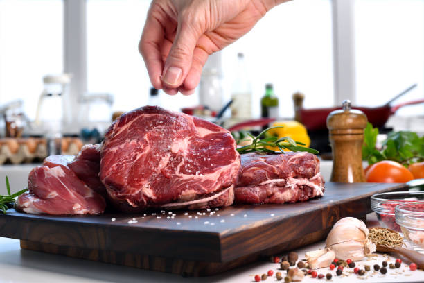 istock Hand sprinkling salt on fresh raw beef meat on a cutting board in the kitchen 1321437231