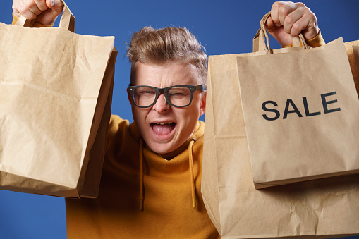 The most vivid and positive emotions on the face of a man who looks out from behind paper bags with purchases that he received with the help of a delivery service from an online store. Shopping online is easy, fun and fast.