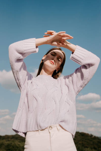 young woman with arms raised standing against sky - blue vertical color image photography imagens e fotografias de stock