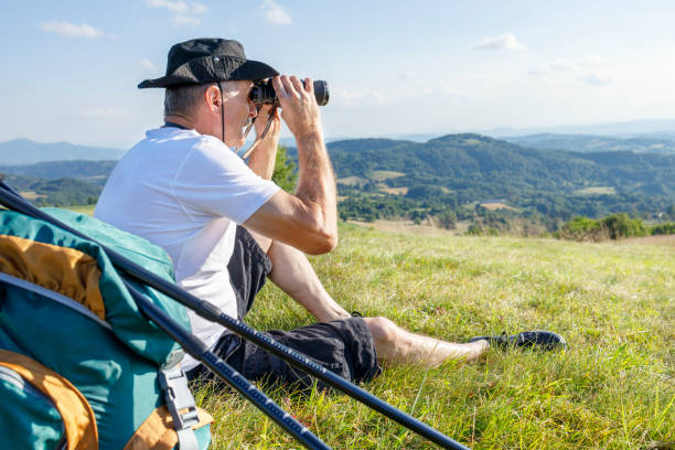 istock Hiker sitting by hiking equipment and using binoculars 1321446101