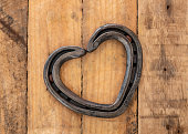 Romantic love heart shaped horse shoe created by farrier laid on rustic vintage wooden plank background.