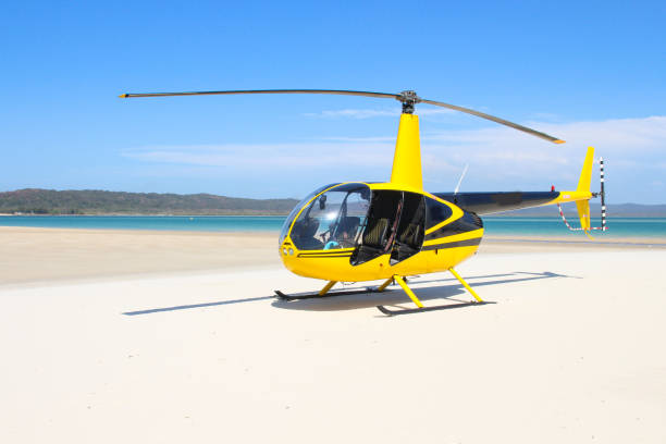 Helicopter yellow and black landed on the white sandy beach with blue body of water in the distance Helicopter landing on the beach helicopter photos stock pictures, royalty-free photos & images