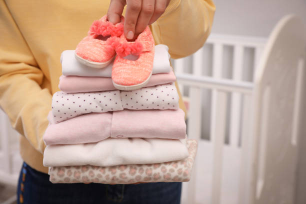 mujer sosteniendo pila de ropa de niña y botines en el interior, primer plano - ropa de bebé fotografías e imágenes de stock