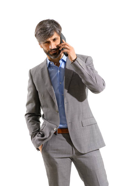 Businessman in stylish suit talking on his smartphone listening with a thoughtful frown to the conversation in a three-quarter portrait isolated over a white studio background