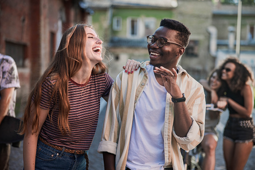 Cheerful black man and his redhead white girlfriend laughing on the street. There are people in the background.