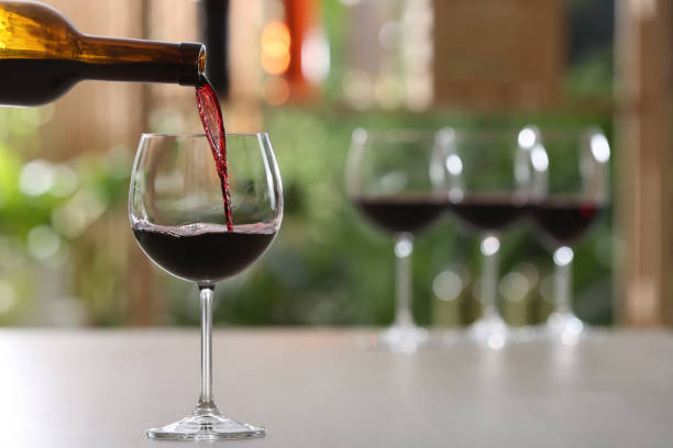 istock Pouring red wine from bottle into glass on table against blurred background, space for text 1321452808