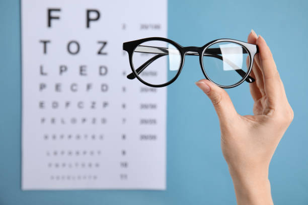 mujer sosteniendo gafas contra la carta de los ojos sobre fondo azul, primer plano. prescripción del oftalmólogo - ophthalmic fotografías e imágenes de stock