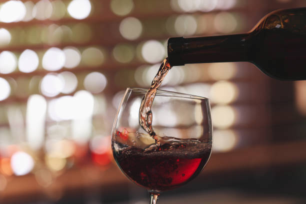 istock Pouring rose wine from bottle into glass on blurred background, closeup 1321453017