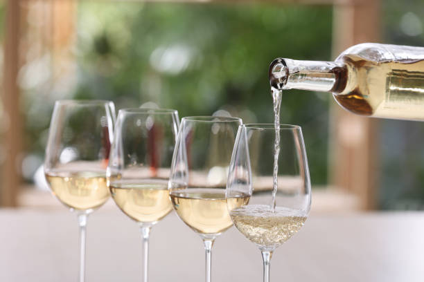 Pouring white wine from bottle into glass on blurred background Pouring white wine from bottle into glass on blurred background white wine photos stock pictures, royalty-free photos & images