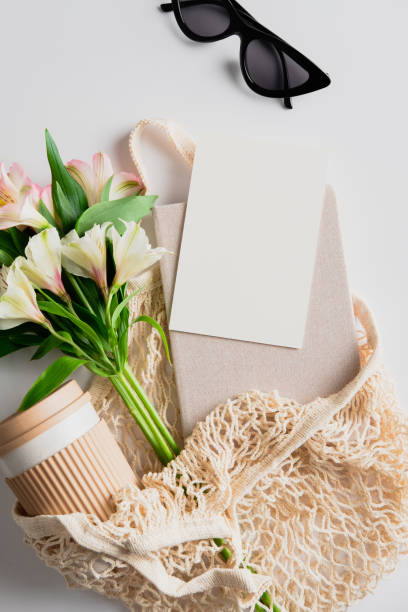istock Eco-friendly string shopping bag with fresh flowers, coffee cup, notebook, blank paper card, glasses. Flat lay, top view. 1321453927