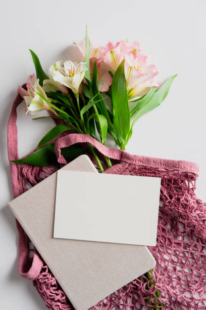 istock Eco-friendly string shopping bag with fresh flowers, paper card mockup, notebook on white table. Flat lay, top view. 1321453928