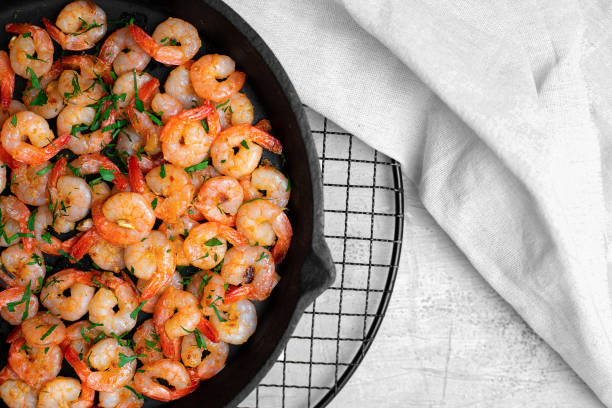 istock Prawns fried with garlic in a cast iron skillet on a white table with a white linen napkin. Top view. 1321455831