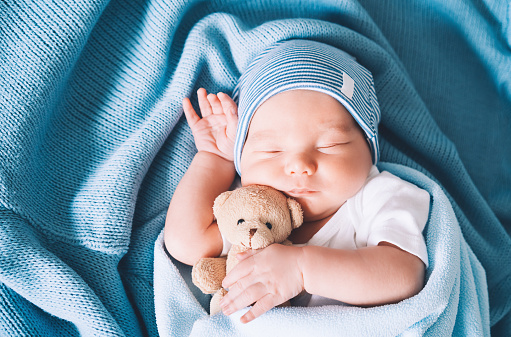 El bebé recién nacido duerme en los primeros días de vida. Retrato del niño recién nacido de una semana de edad durmiendo plácidamente con un lindo juguete suave en cuna en fondo de tela. photo