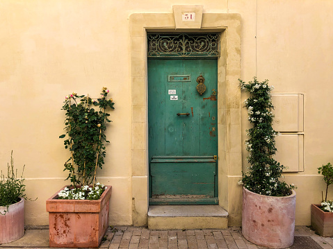 Horizontal closeup of the front facade of a traditional house in the old centre of Arles with a green painted front door and two pot plants