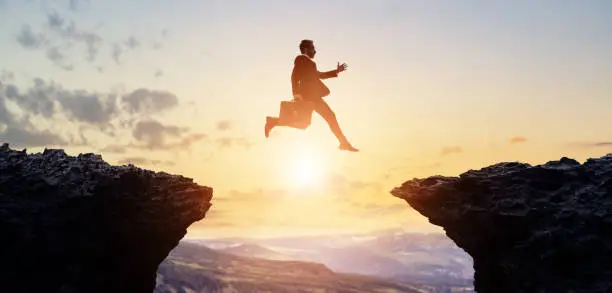 Challenge of business concept. A businessman jumping over a valley.