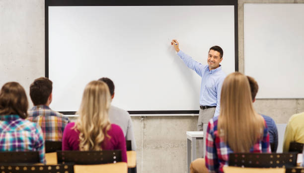 group of students and smiling teacher in classroom education, high school, teamwork and people concept - smiling teacher standing in front of students and writing something on white board in classroom teacher projector stock pictures, royalty-free photos & images