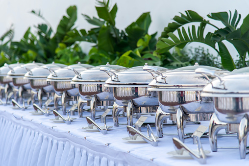 Large number of warm dishes in catering Chafing dish containers in a raw ready for upcoming guests to the buffet restaurant