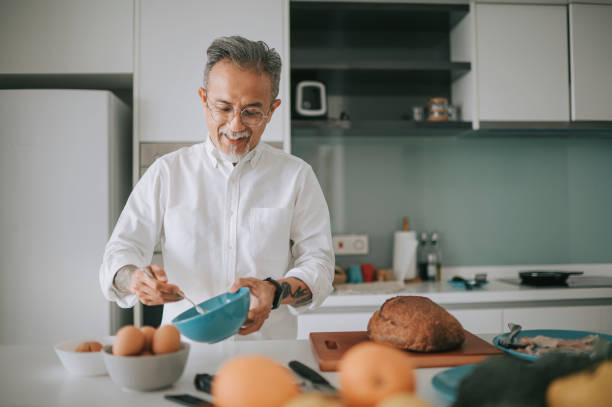 азиатский китайский седые волосы старший мужчина волосы стерни перемешивания яйцо йорк приготовления пищи на домашней кухне выходные - smart casual occupation casual healthy eating стоковые фото и изображения