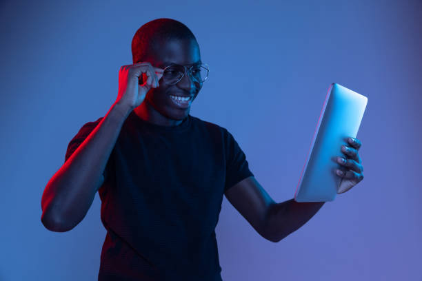 istock Happy young African handsome man with tablet isolated over dark background in mixed neon light. 1321470634