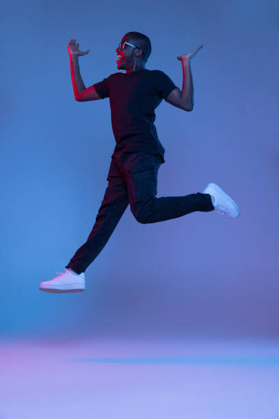 istock Young African handsome man jumping isolated over dark background in mixed neon light. Flyer 1321470682