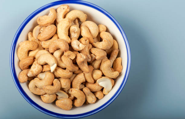 плоды кешью в белой миске на синем фоне. вид сверху. - cashew close up food salted стоковые фото и изображения
