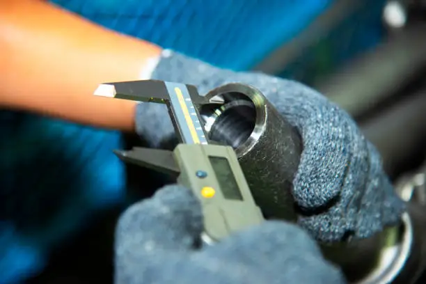 Photo of Hand of technician wearing cloth gloves was using a digital vernier tool to measure the width