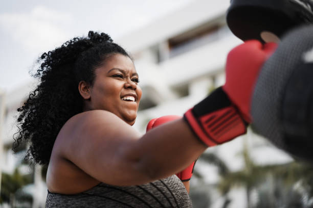 Curvy woman and personal trainer doing boxing workout session outdoor - Focus on face Curvy woman and personal trainer doing boxing workout session outdoor - Focus on face boxing gym stock pictures, royalty-free photos & images