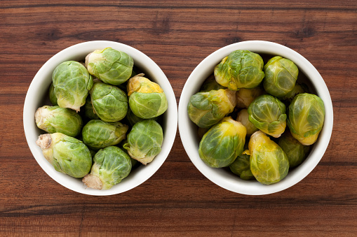 Two bowls containing raw and boiled brussels sprouts