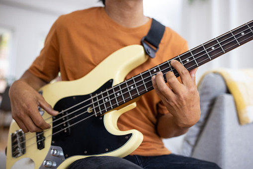 Unrecognizable man playing bass guitar at home