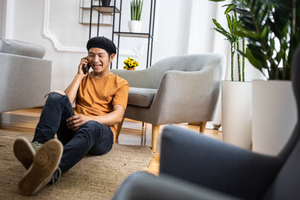 istock Japanese man laughing and having fun conversation with his friend using smart phone from living room at home 1321486720