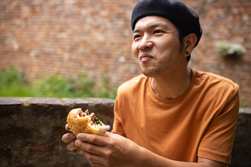 Japanese man enjoying the taste of delicious burger at backyard