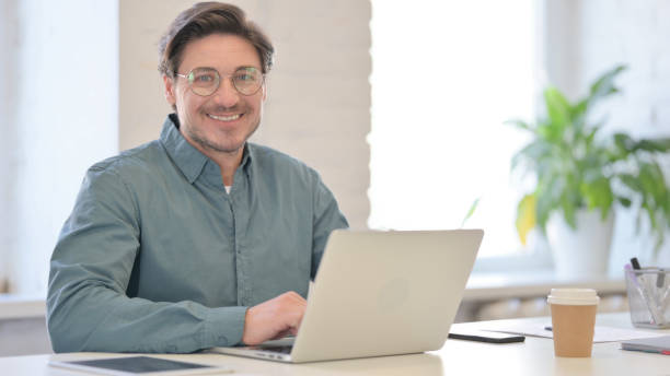 istock Middle Aged Man with Laptop Smiling at Camera 1321491131