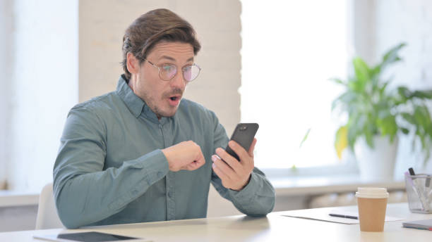 istock Middle Aged Man Reacting to Loss on Smartphone in Office 1321491182