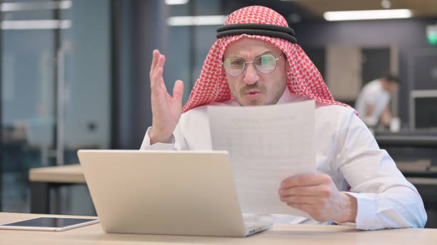 Middle Aged Man with Laptop Reacting to Loss Documents The Middle Aged Man with Laptop Reacting to Loss Documents middle eastern ethnicity mature adult book reading stock pictures, royalty-free photos & images