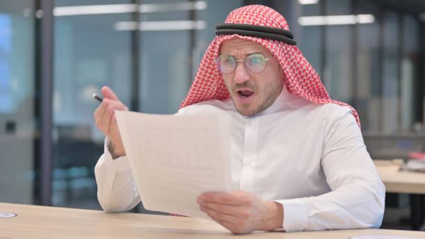 Middle Aged Man Reacting to Loss While Reading  Documents The Middle Aged Man Reacting to Loss While Reading  Documents middle eastern ethnicity mature adult book reading stock pictures, royalty-free photos & images