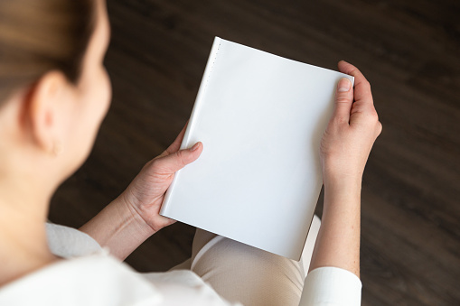 beautiful female hands holding white magazine with blank cover mock up at home