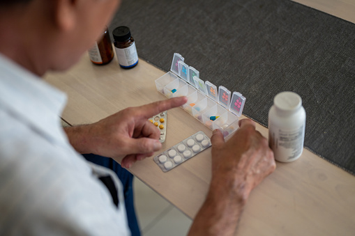 An Asian senior man is putting pills into an organizer with the tablets and bottles around the table at home.