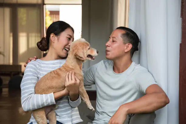 Photo of Diversity young couple Play with his dog in the house. They are hugging their little puppy