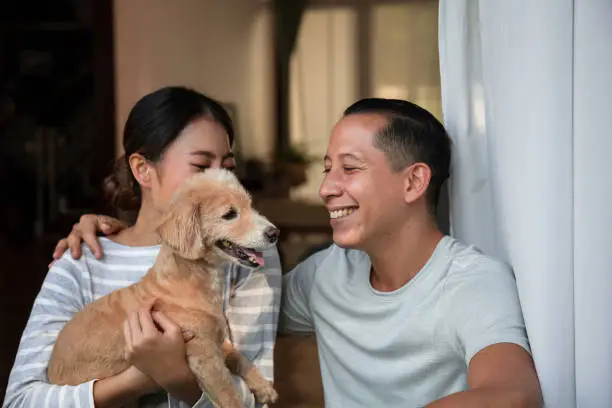 Photo of Diversity young couple Play with his dog in the house. They are hugging their little puppy