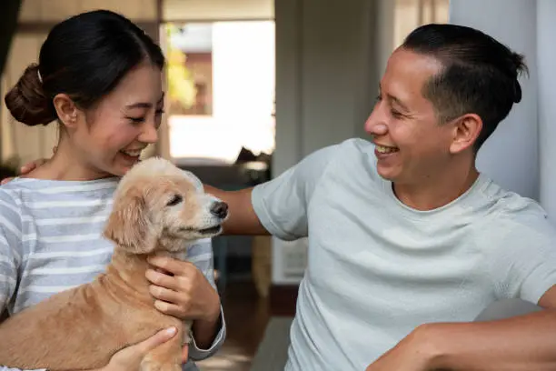 Photo of Diversity young couple Play with his dog in the house. They are hugging their little puppy